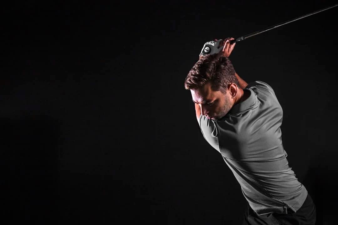 Golfer mid-swing in an atmospheric TrackMan simulator bay with moody dark lighting